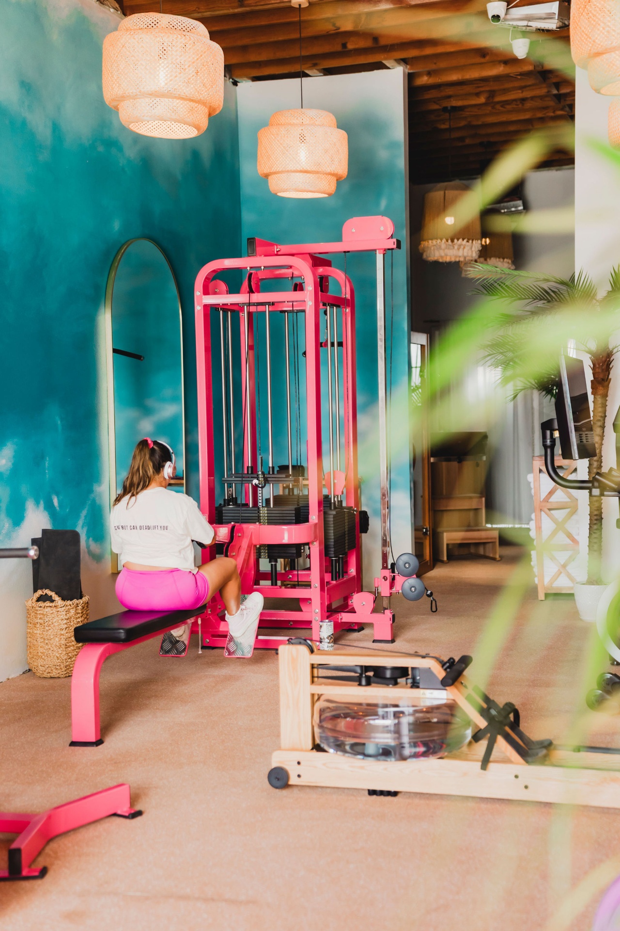 Member training on pink cable machine beside turquoise mural